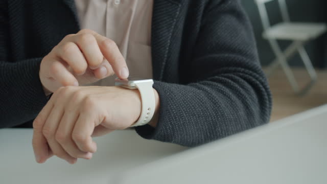 Close-up-of-man's-hand-using-digital-smart-watch-touching-screen-in-office
