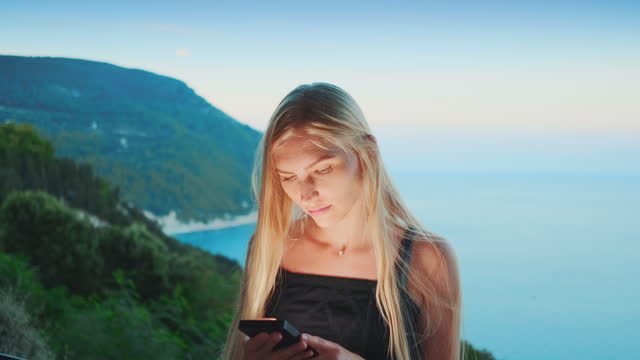 Mujer-rubia-usando-el-teléfono-inteligente-con-el-océano-en-el-fondo
