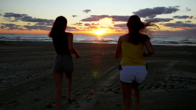 Freundinnen-bei-Sonnenaufgang-am-Strand-in-Richtung-Meer-laufen