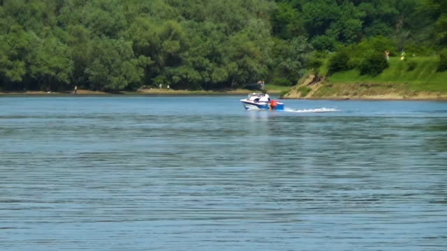 Eine-Motorboot-mit-drei-Passagieren-fährt-entlang-des-Flussufers