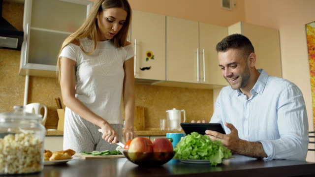 Attractive-couple-chatting-in-the-kitchen-early-morning.-Beautiful-woman-feed-her-husband-while-cooking-breakfast