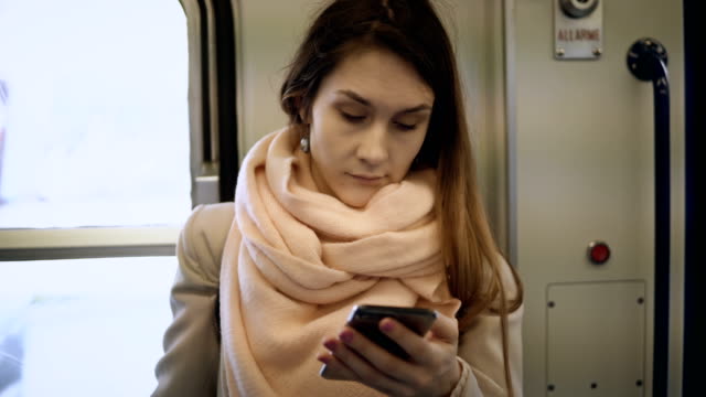 Young-attractive-woman-standing-in-metro-and-using-the-smartphone.-Brunette-female-surfing-the-Internet-in-train