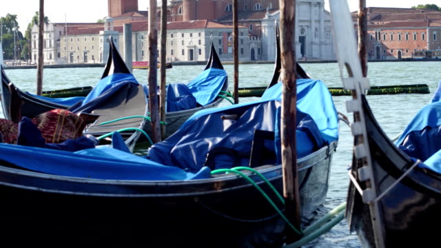 Moored-Venetian-gondolas-swaying-against-cityscape.-Venice,-Italy