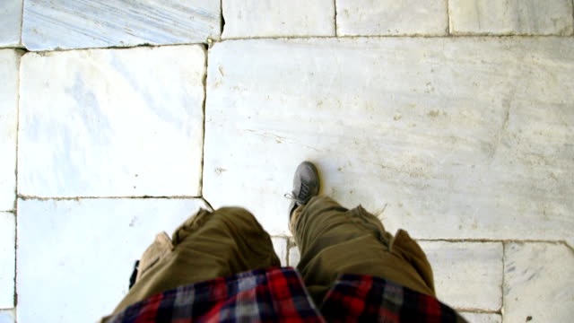 Vista-punto-de-vista-del-hombre-en-zapatillas-de-deporte-caminando-acera-antigua-histórica-superior