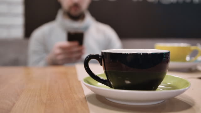 Eine-nicht-erkennbare-Mann-sitzt-im-Restaurant-und-nutzen-das-Smartphone-in-die-Unschärfe-von-einer-Tasse-Tee.-Slow-motion