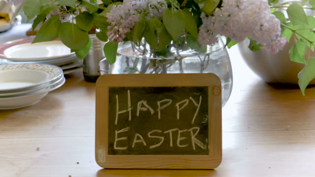 Frohe-Ostern,-geschrieben-auf-einer-kleinen-Tafel-gegen-eine-Vase-mit-schönen-Blumen