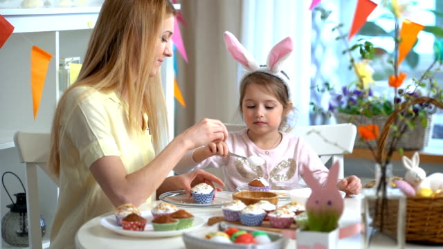 Joven-madre-y-su-hija-con-orejas-de-conejo-cocinar-cupcakes-de-Pascua