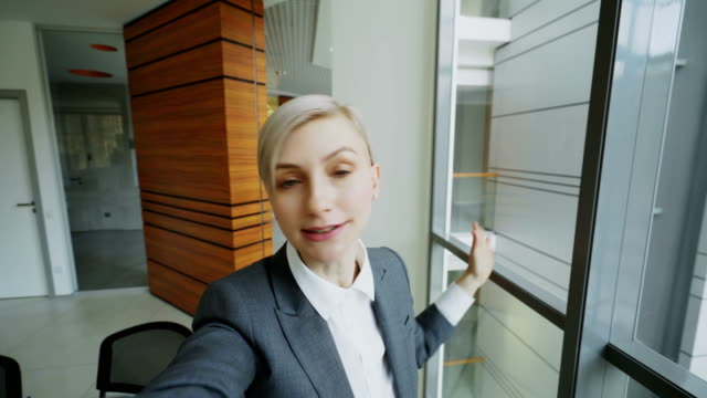 POV-of-young-businesswoman-in-suit-having-online-video-chat-using-smartphone-camera-and-talking-to-his-colleagues-in-modern-office