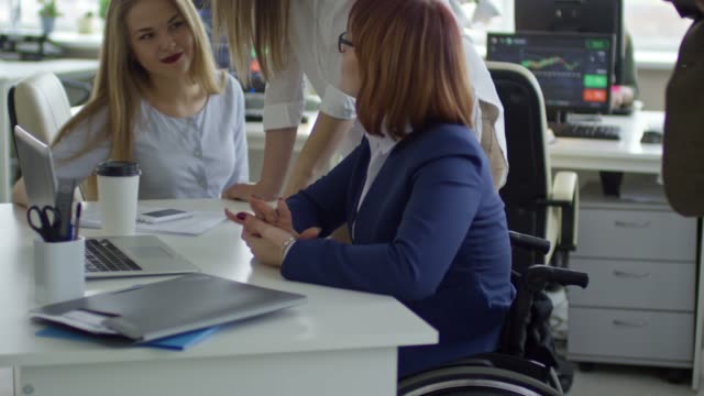 Handicapped-Business-Lady-Speaking-to-Female-Colleagues-in-Office