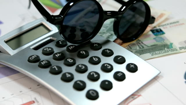 Sun-protective-hipster-glasses-lie-on-the-calculator-and-rubles.-Rotation