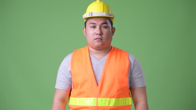 Schönen-übergewichtigen-jungen-asiatischen-Mann-Bauarbeiter-vor-grünem-Hintergrund