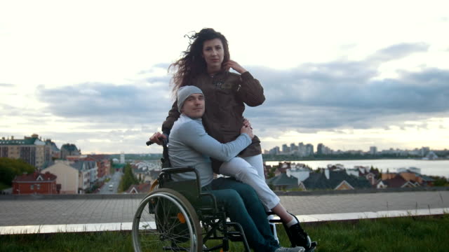 Porträt-von-einem-glücklichen-behinderten-Menschen-im-Rollstuhl-umarmt-mit-Mädchen-im-freien