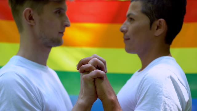 Homosexual-men-kissing-on-rainbow-flag-background,-society-tolerance,-community