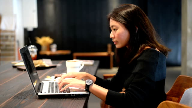 Asian-woman-working-on-laptop-and-drinking-coffee-in-cafe