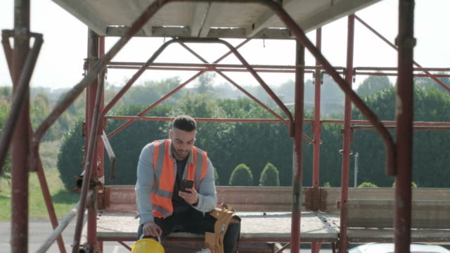 Man-Working-In-Construction-Site-Smiling-And-Using-Smartphone