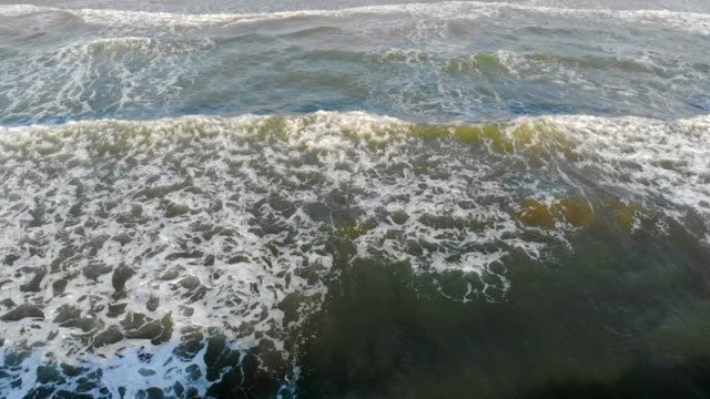 Las-olas-del-mar-Mediterráneo-vienen-a-la-costa,-la-cámara-sube-lentamente-y-muestra-la-ciudad-de-Valencia