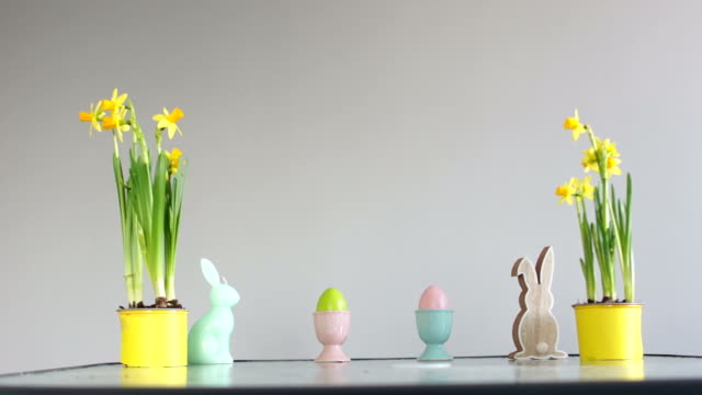 Ostern-Dekoration-auf-dem-Tisch.-Kinderhände-entführen-dekorierte-Eier.-Eingemachte-Narzissen,-Kaninchen-Figur