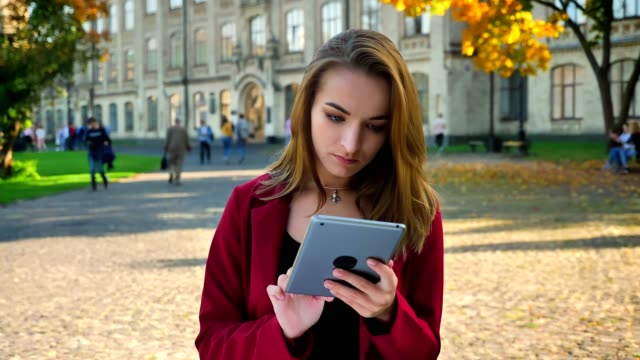 Beautiful-young-girl,-student-browsing,-messaging-on-the-tablet,-gets-frustrated-and-then-amused,-outside-the-university