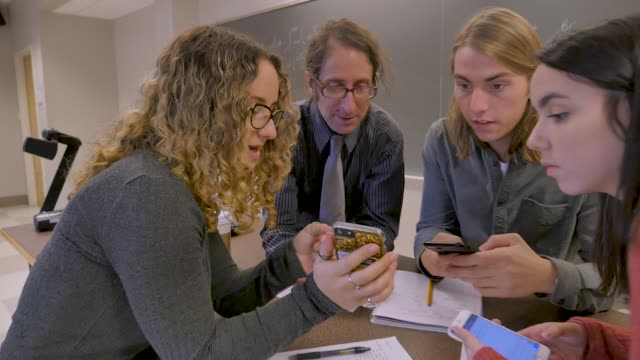 Estudiante-femenina-mostrando-a-su-maestra-y-compañeros-de-clase-algo-en-su-teléfono-móvil