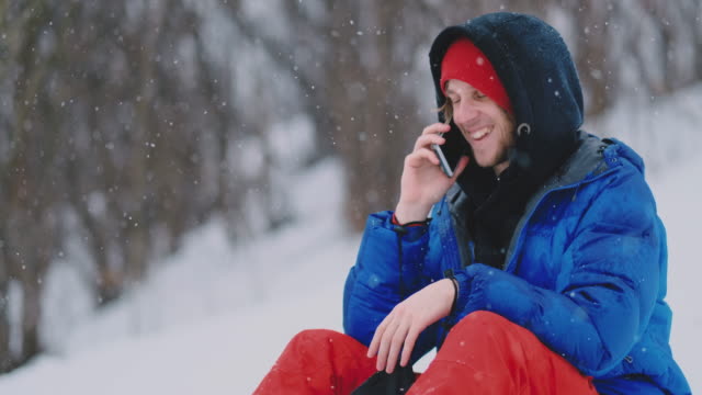 Un-snowboarder-masculino-sentado-en-la-nieve-toma-fotos-en-el-teléfono-de-un-hermoso-paisaje-turístico-para-las-redes-sociales.-Resort-blogger