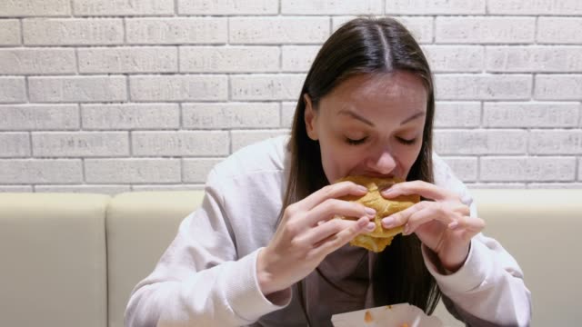 Mujer-comiendo-una-hamburguesa-con-gusto-y-deleite-en-la-cafetería.
