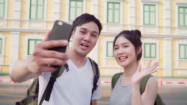 Asian-blogger-couple-travel-in-Bangkok,-Thailand,-sweet-couple-using-mobile-phone-make-vlog-and-live-in-social-media-while-spending-sweet-time-in-holiday-trip.-Couple-travel-in-city-concept.