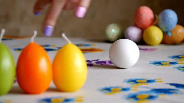 Easter.-Female-hand-spin-white-egg-on-the-table.-Colorful-Easter-eggs-in-the-background.