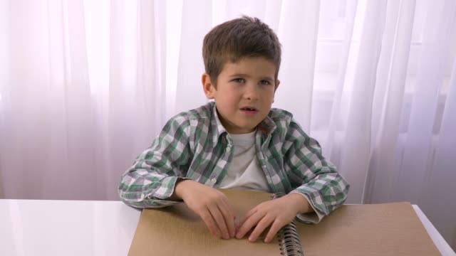 Visually-impaired-small-boy-reading-braille-book-with-symbols-font-for-blind-sitting-at-table