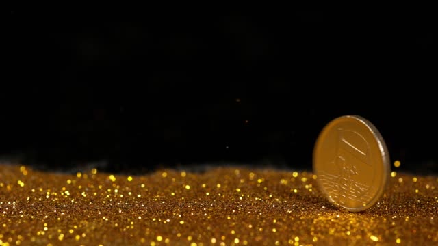 Münze-von-1-Euro-Rolling-auf-Goldpulver-gegen-schwarzen-Hintergrund,-Slow-motion-4K