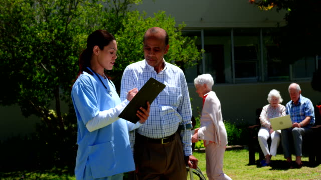 Vista-frontal-del-hombre-Senior-asiático-activo-y-médico-femenino-discutiendo-sobre-informe-médico-en-el-jardín