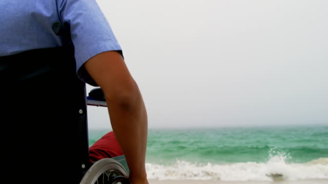 Blick-auf-den-Afroamerikaner,-der-auf-dem-Rollstuhl-sitzt,-am-Strand-4k