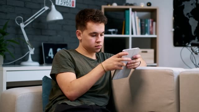 Portrait-view-of-a-young-guy-sitting-on-the-couch-and-sufring-the-web-on-his-tablet