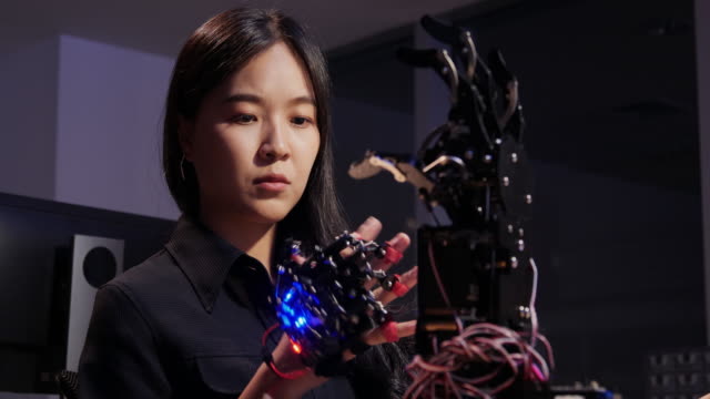 Asiatische-Tests-Cyborg-Hand-im-Kontrollraum.-Weiblich,-die-ihr-Roboterprojekt-macht,-testet-sensorsignal.-Technologie--und-Innovationskonzept.