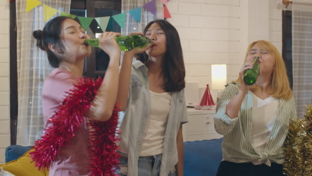 Gruppe-von-asiatischen-Frauen-Party-zu-Hause,-weibliche-trinken-Bier-tanzen-und-singen-lustig-zusammen-im-Wohnzimmer-in-der-Nacht.-Teenager-junge-Freunde-spielen-Spiel,-feiern-Urlaub-Konzept.-zeitlupe.