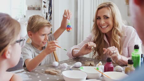 Family-sitting-around-kitchen-table-with-parents-helping-children-to-paint-eggs-for-Easter---shot-in-slow-motion