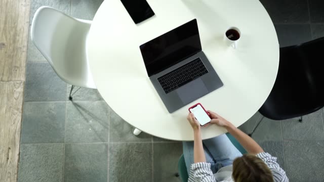 Top-Ansicht-von-jungen-Millennial-Hipster-Mädchen-mit-modernen-Technologien-für-die-Vernetzung,-während-zu-Hause-Innentisch-mit-Laptop-Computer-sitzen-und-mit-Dem-Smartphone-zum-Chatten