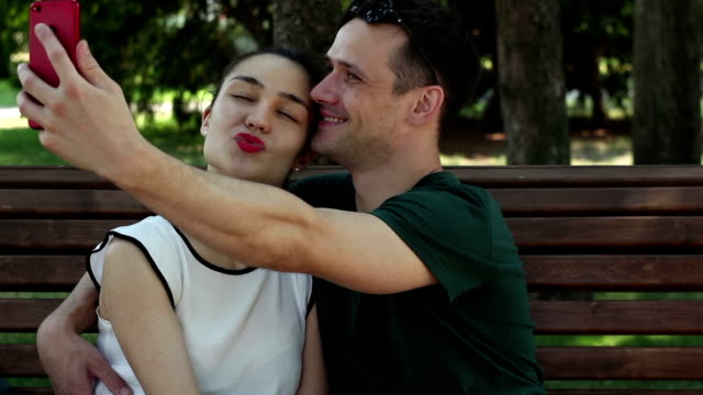 Young-couple-in-love-is-photographed-sitting-on-a-bench-in-the-park.They-are-smiling-and-hugging-each-other.
