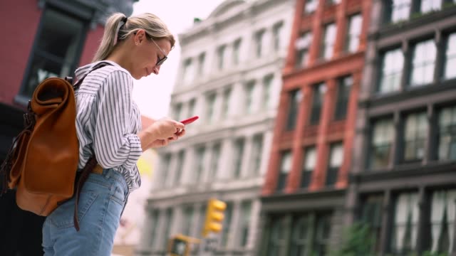Attractive-millennial-woman-traveller-in-stylish-apparel-making-online-booking-of-hotel-via-cellphone-app-connected-to-4g-wireless-during-sightseeing-around-city-streets