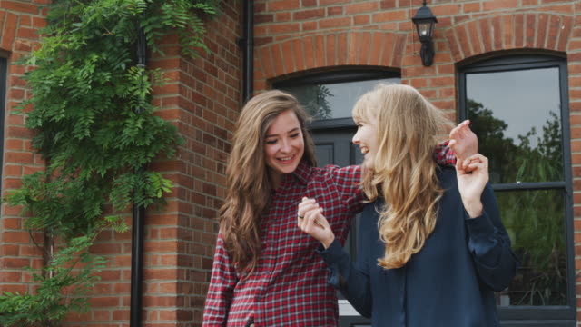 Portrait-Of-Excited-Gay-Female-Couple-Standing-Outside-New-Home-Holding-Keys-Together