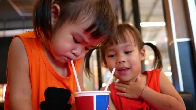 Kleines-asiatisches-Mädchen-mit-ihrer-Schwester-nippt-ihr-Getränk-zusammen,-während-sitzen-warten-Essen-im-Restaurant.-Selektiver-Fokus.