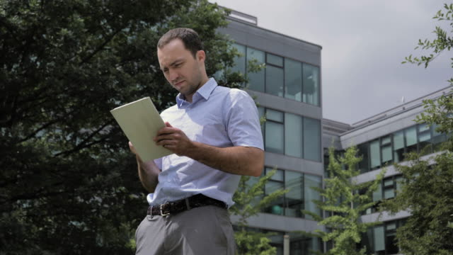Businessman-standing-in-city-park,-near-office-buildings-using-tablet