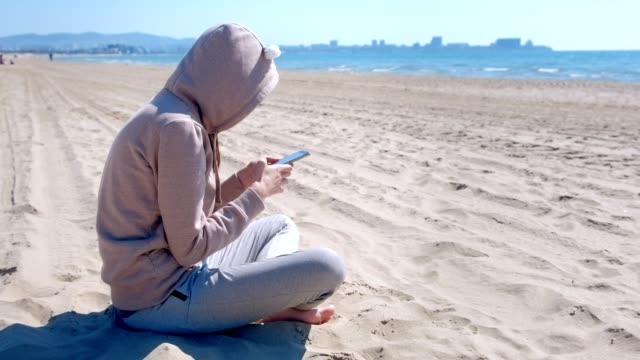 Mujer-irreconocible-está-escribiendo-por-teléfono-sentado-en-la-playa-del-mar.