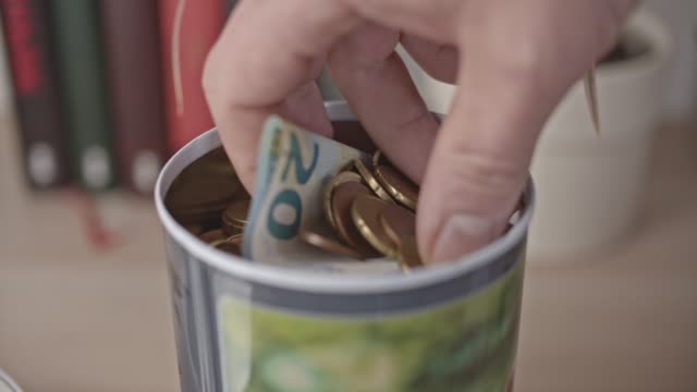 Männliche-Hand-nimmt-eine-Handvoll-Euro-Münzen-und-Banknote-aus-einem-Glas