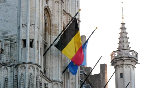 Hohes-historisches-Gebäude-mit-aufsteigenden-Flaggen-Belgiens-und-der-Europäischen-Union-in-slo-mo
