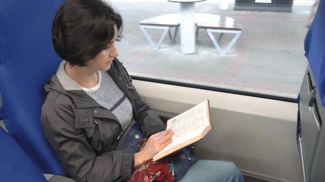 Mujer-caucásica-se-sienta-en-tren-por-ventana-Leendes-libro-Tren-paradas-de-tren-en-la-plataforma