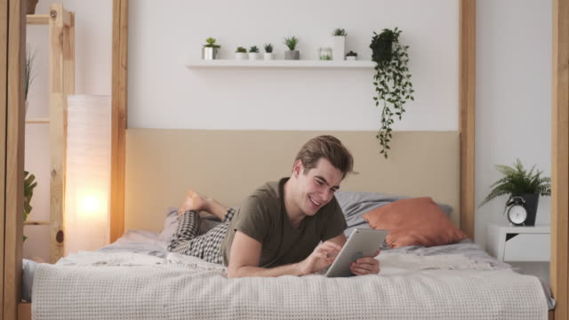 Zufriedener-Mann-mit-digitalen-Tablet-im-Bett-zu-Hause