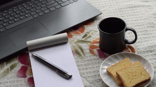 Frühstückskaffee-im-Morgensonnenschein-mit-Laptop-Computer-schwarz-Farbstift-und-weiß-regiert-Papier-Notebook,-Keramik-Tasse-Untertasse-und-Keks-auf-Top-Büro-Platz-Schreibtisch-Hintergrund.-Lifestyle-Image.