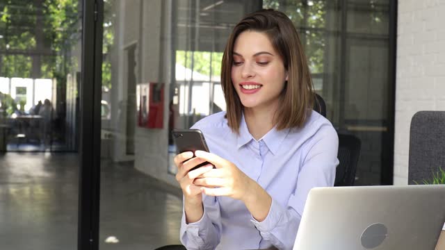 Funny-euphoric-young-woman-texting-message-on-smartphone-at-modern-office.-Excited-girl-receive-read-good-news-on-cellphone.