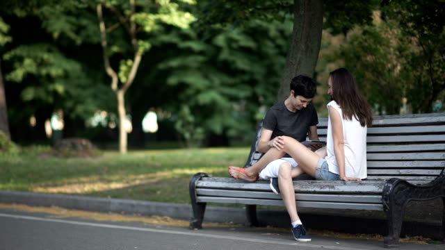 Zwei-Lesben-Tablet-nutzen-und-entspannen-Sie-sich-auf-eine-Bank-im-park