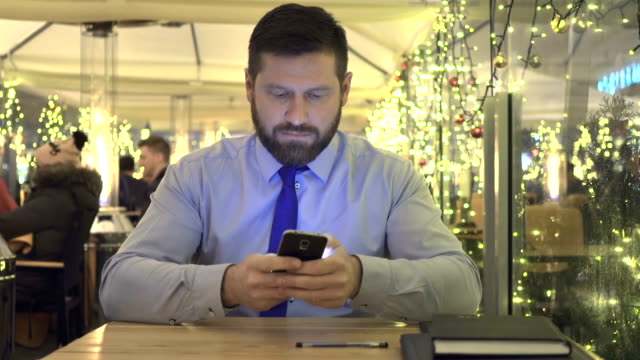 Hombre-de-negocios-sms-escribiendo-con-aplicación-para-smartphone,-de-noche,-café,-portriat,-Navidad